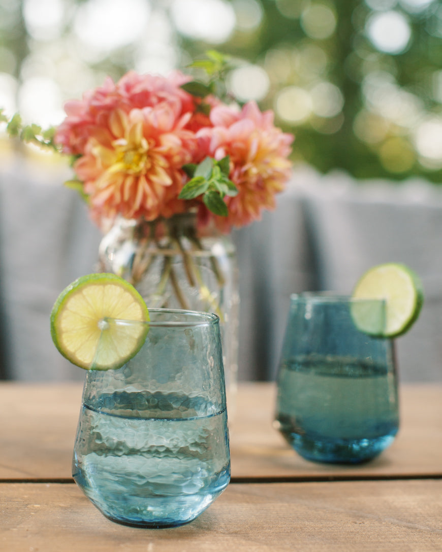 Two blue glasses with lime slices on a wooden table with a blurred floral background