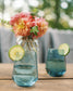 Two blue glasses with lime slices on a wooden table with a blurred floral background