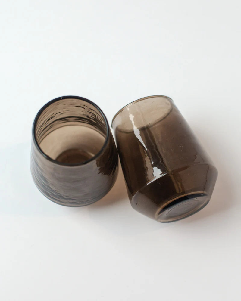 Two dark brown glass tumblers on a white background