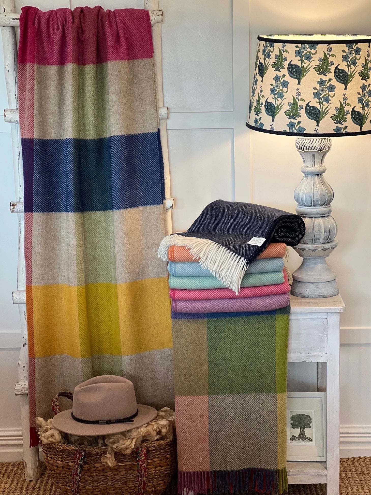 Colorful plaid blanket draped over a radiator with folded blankets and a lamp in the background.
