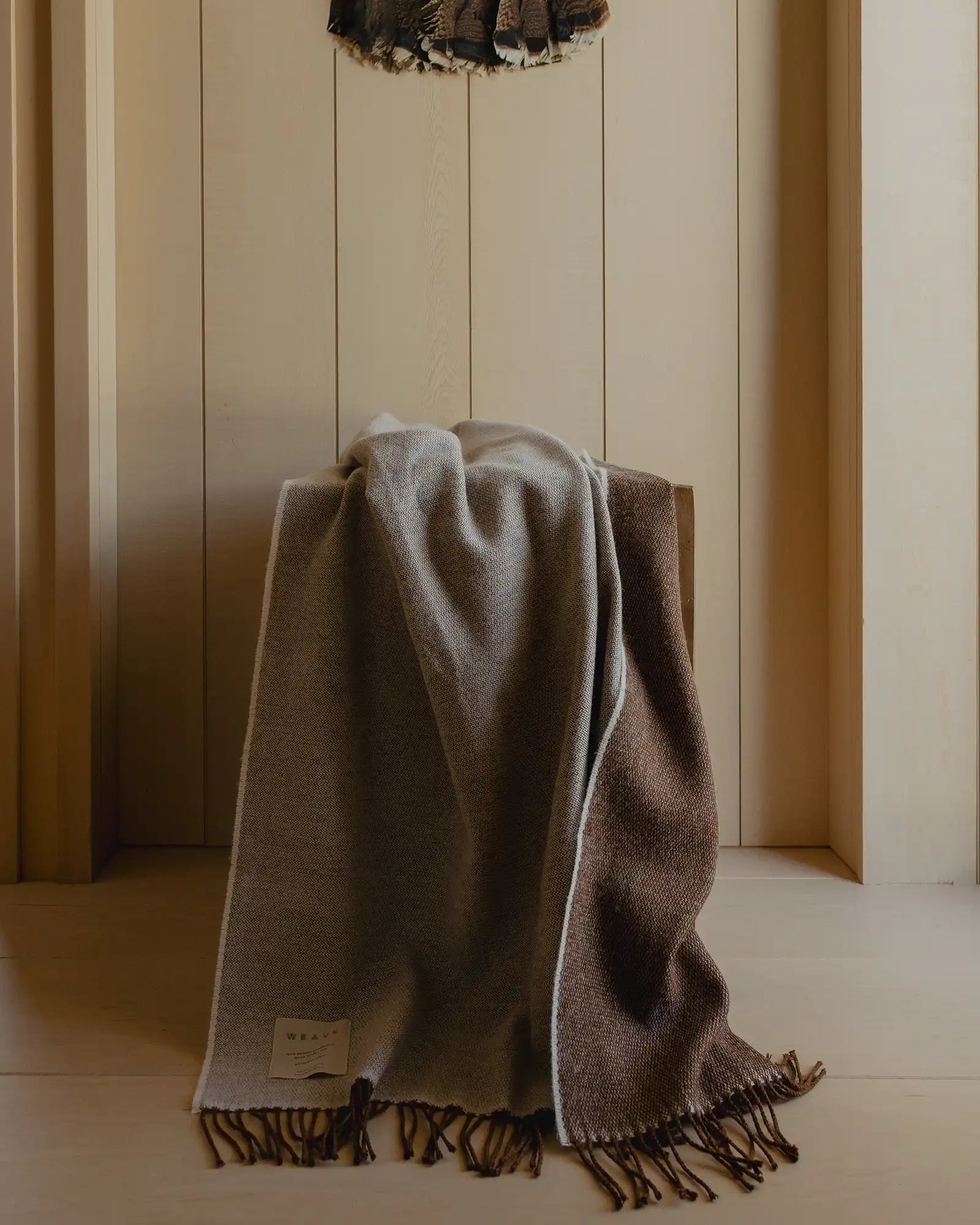 Brown blanket with tassels draped over a chair against a wooden paneled wall.