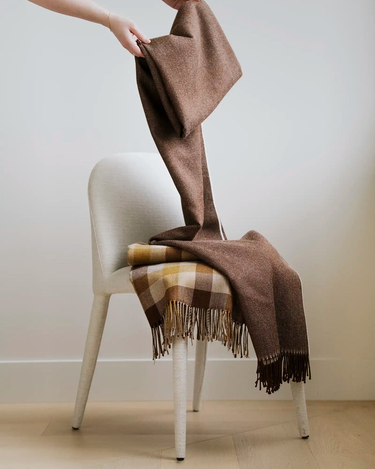 Brown plaid blanket draped over a white chair against a plain background