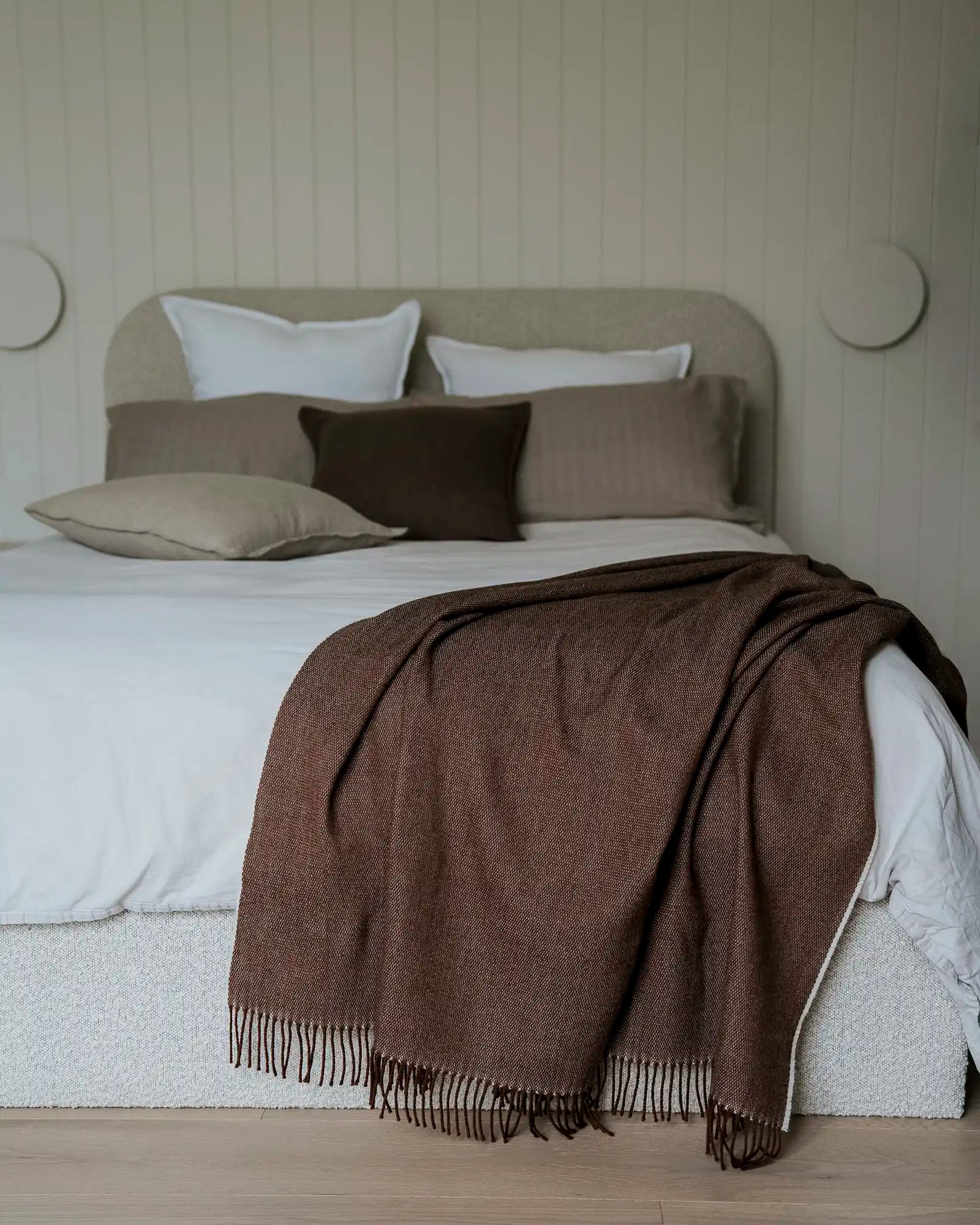 Bed with brown blanket and pillows against a neutral wall