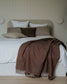 Bed with brown blanket and pillows against a neutral wall