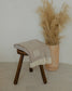Beige blanket draped over a wooden stool next to a vase with dried plants on a neutral background