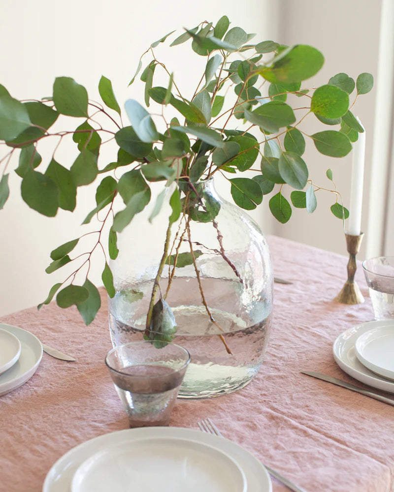 Clear vase with green leaves on a table setting with pink tablecloth