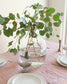 Clear vase with green leaves on a table setting with pink tablecloth