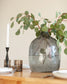 Decorative vase with greenery on a table with candles and plates.