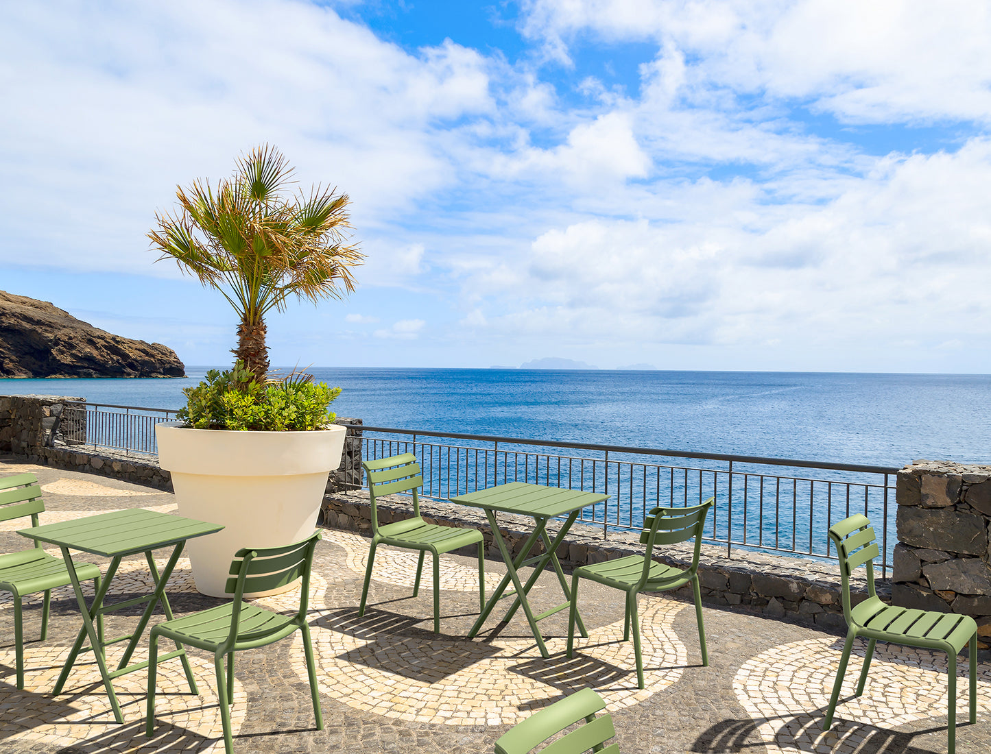Outdoor seating area with green tables and chairs by the ocean
