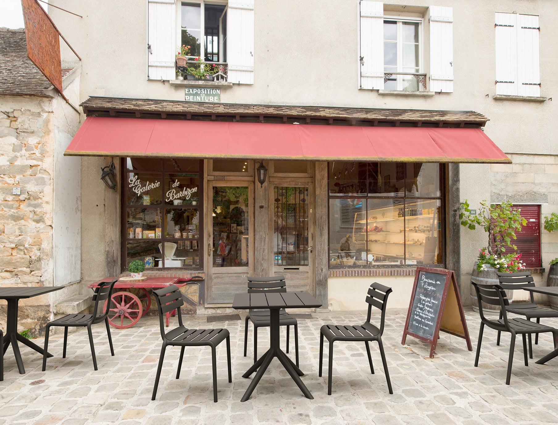 Outdoor seating area in front of a store with tables, chairs, and a red awning.