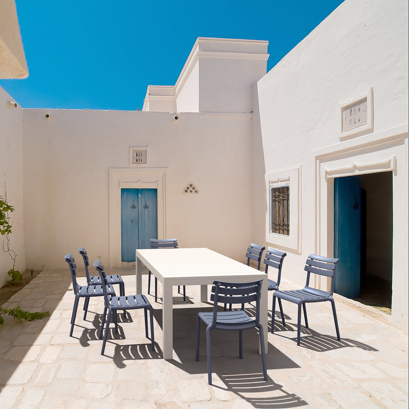 White building exterior with a blue door and outdoor dining area.