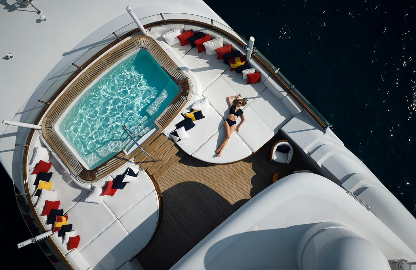 Person lounging by a pool on a yacht deck with a clear sky.