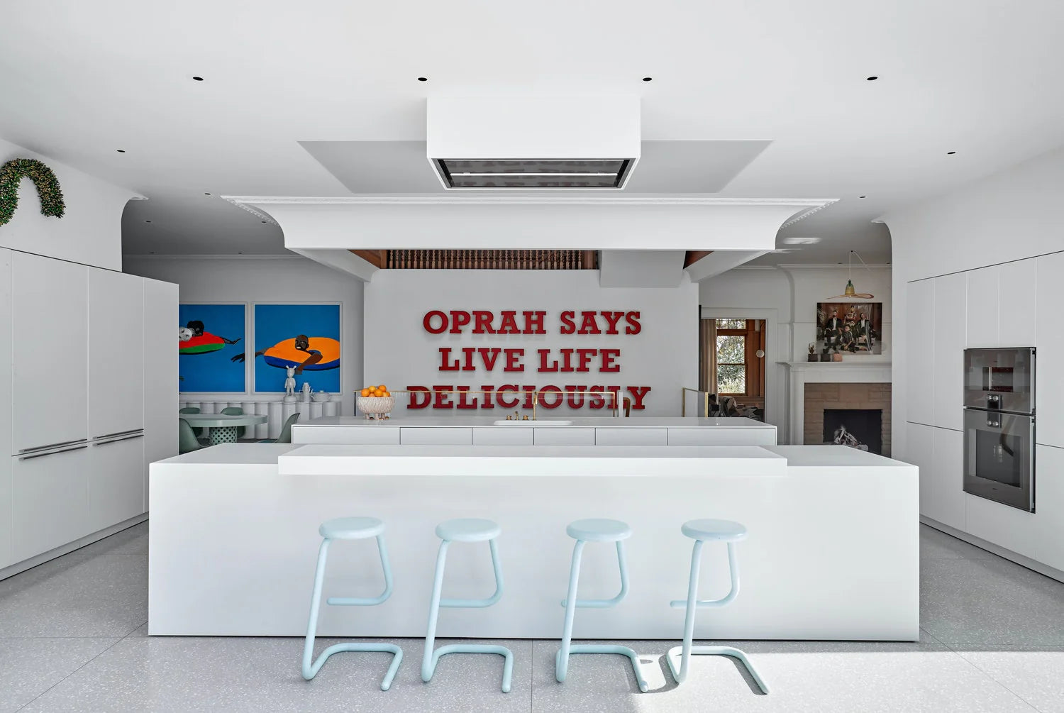 Modern kitchen with a quote on the wall, featuring white cabinetry and a central island.