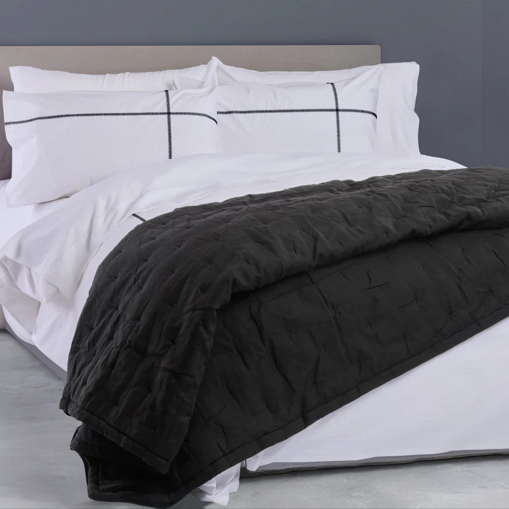 Bed with white bedding and black quilt on a gray bed frame.