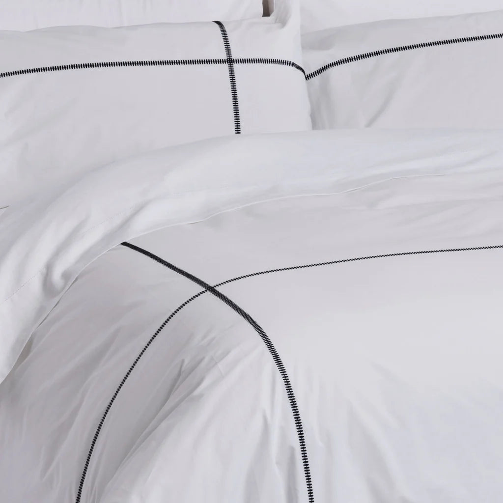 White bedding set with black piping on a plain background