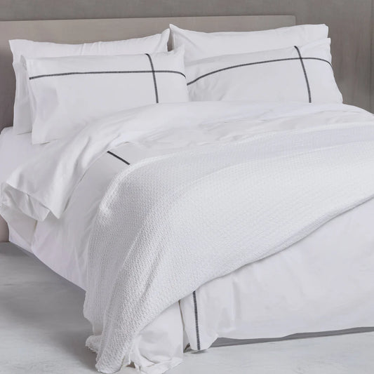 White bedding set with black piping on a bed in a neutral room.
