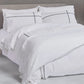 White bedding set with black piping on a bed in a neutral room.