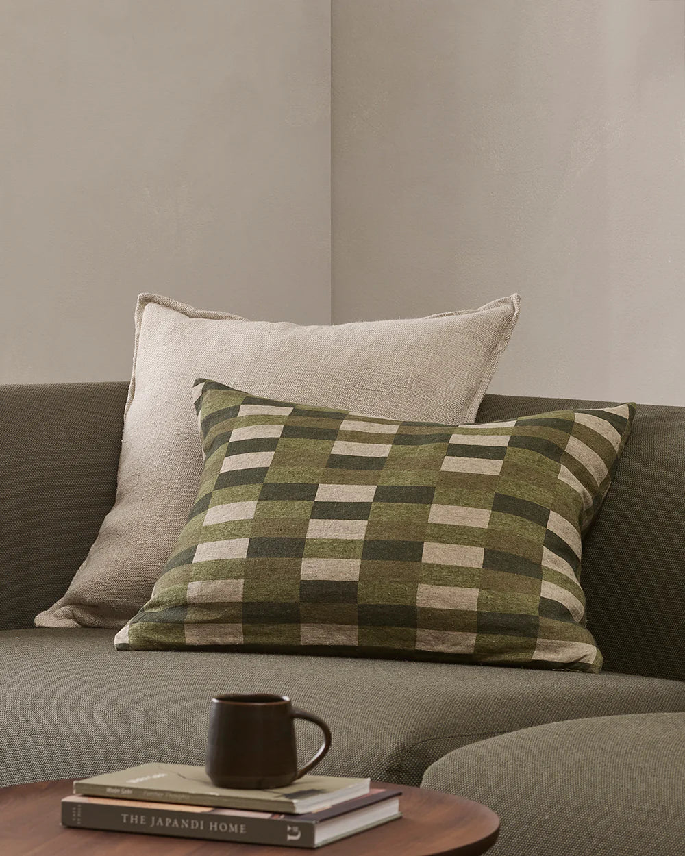 Checkered pillow on a sofa with a cup and books on a small table.