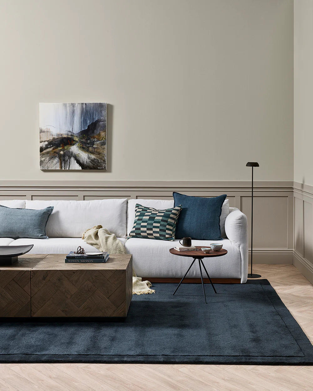 Modern living room with a white sofa, wooden coffee table, and abstract painting on the wall.