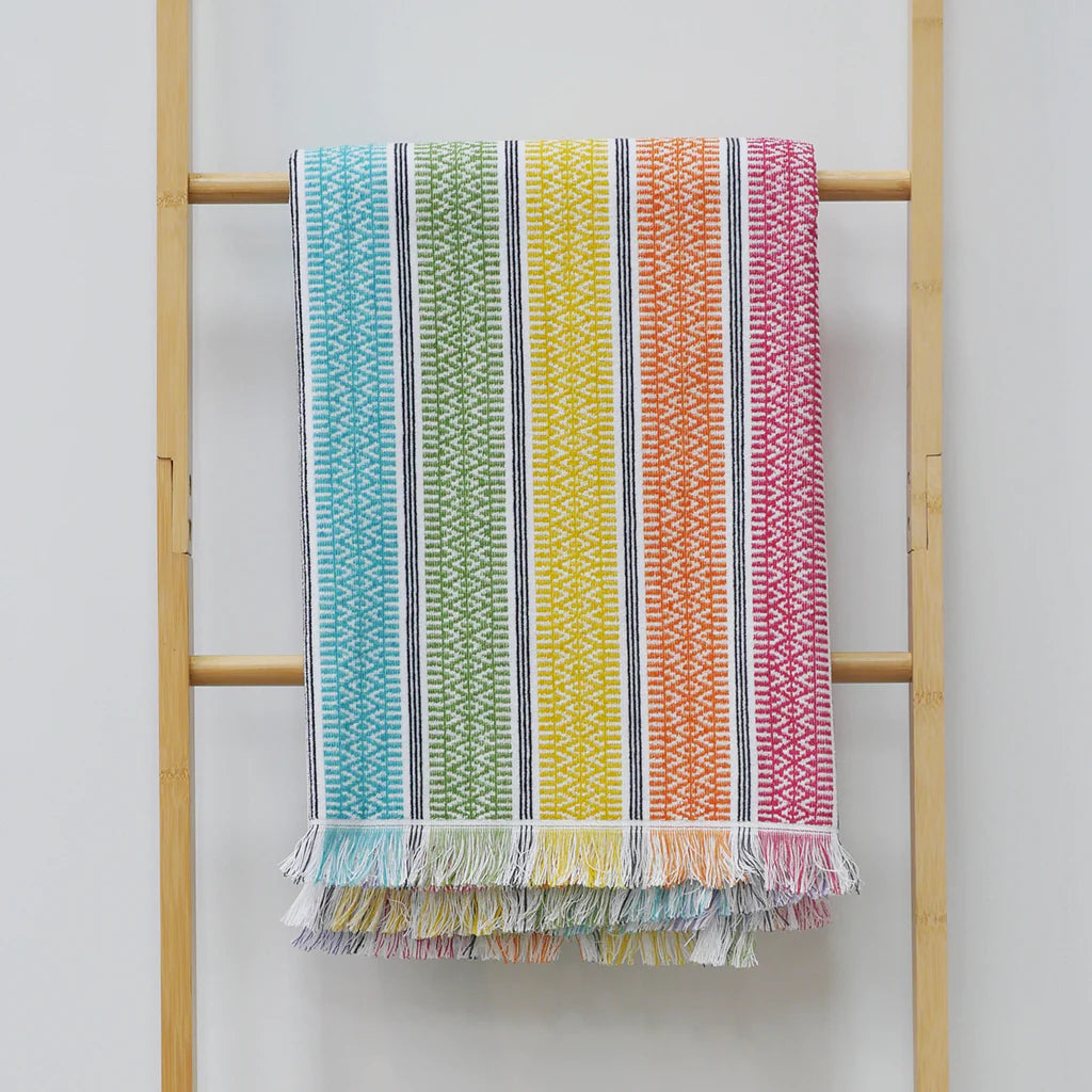 Striped indiie beach towel handing on a rail in blue green yellow orange and pink