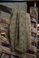 A woven throw blanket with a geometric chevron pattern in olive green and beige, draped over a rustic wooden fence.