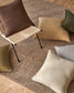 Chair with brown cushion on a textured floor with various pillows.