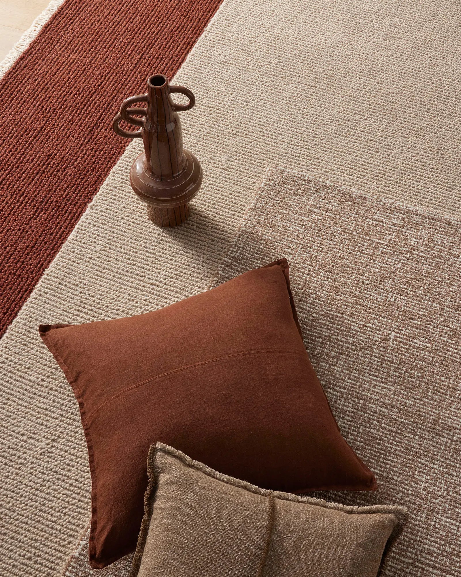 Brown pillow and decorative vase on a textured beige and red rug