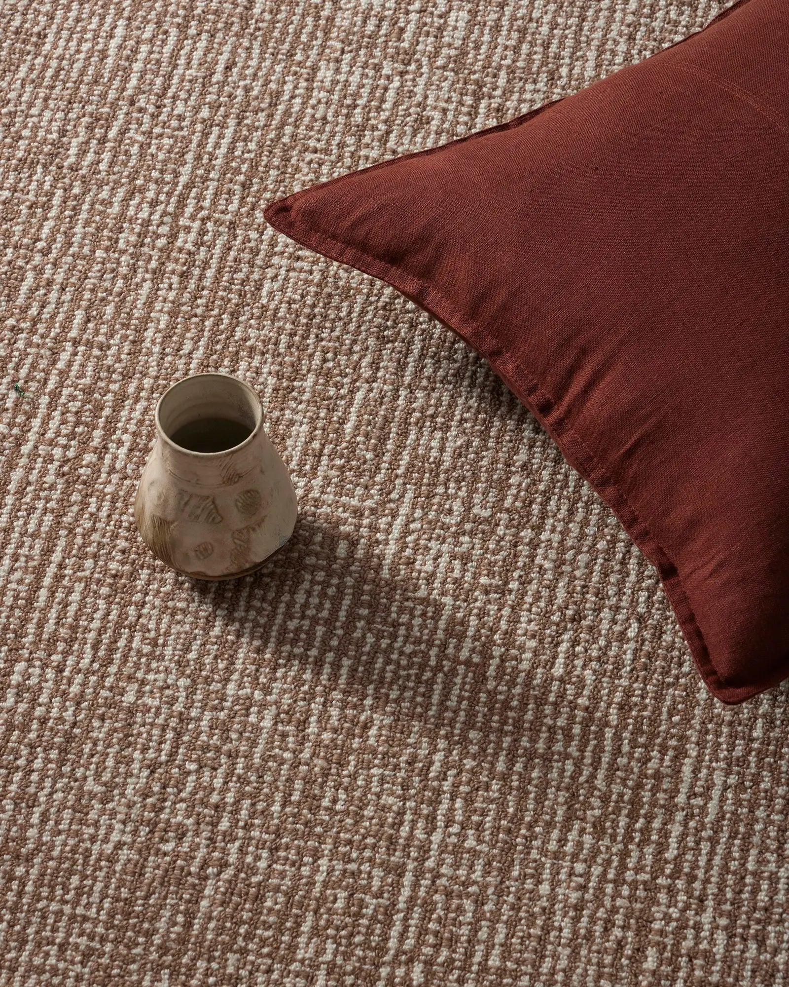 Ceramic vase and red pillow on a textured carpet