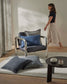 Woman walking past a modern chair with blue cushions in a minimalistic room.