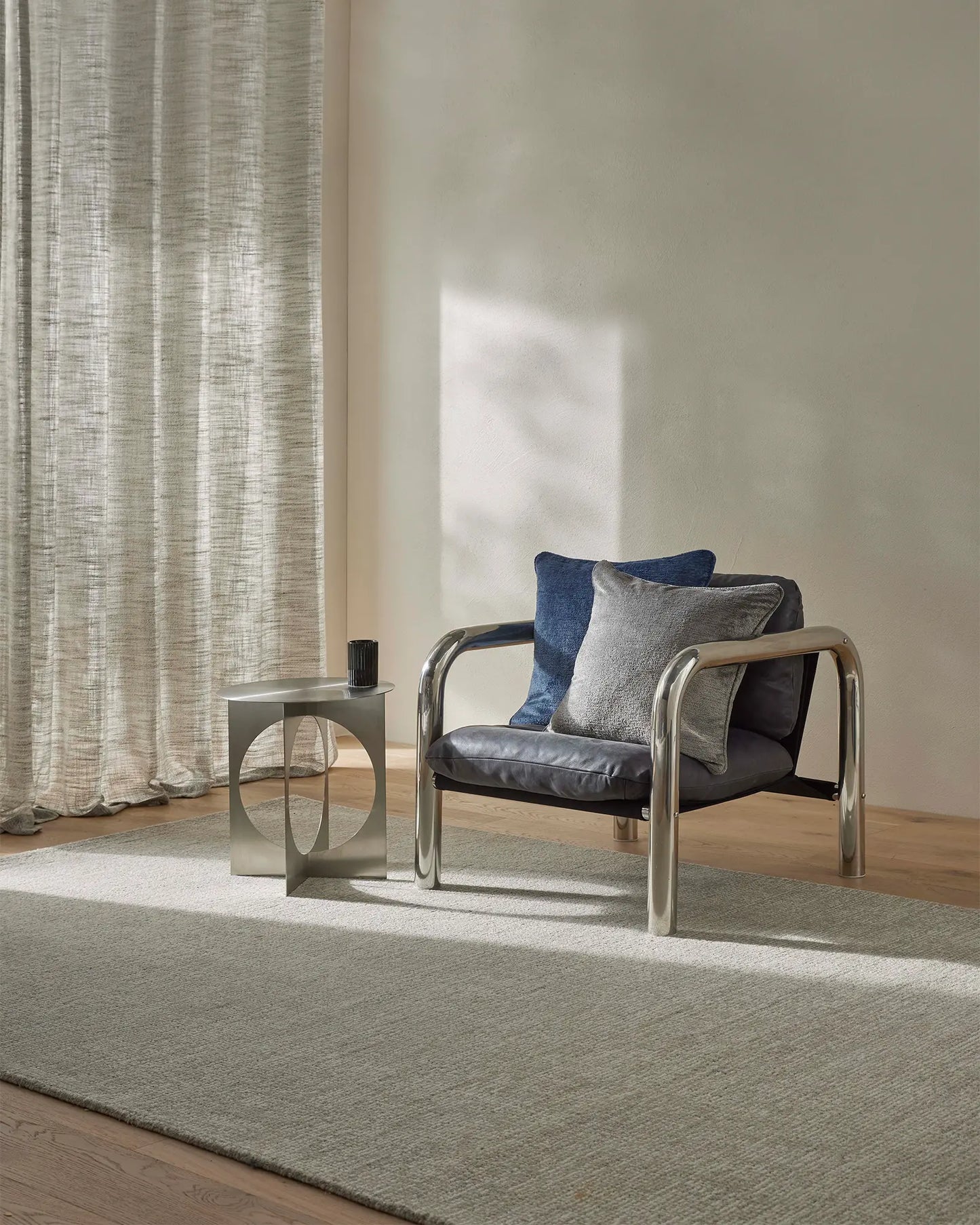 Modern chair with blue and gray cushions in a room with curtains and a rug.