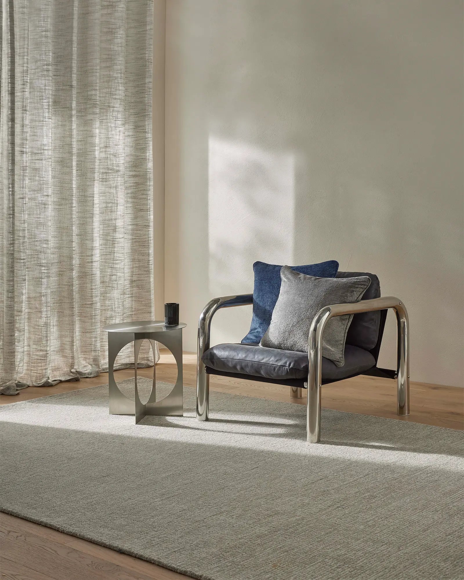 Modern chair with blue and gray cushions in a room with curtains and a rug.