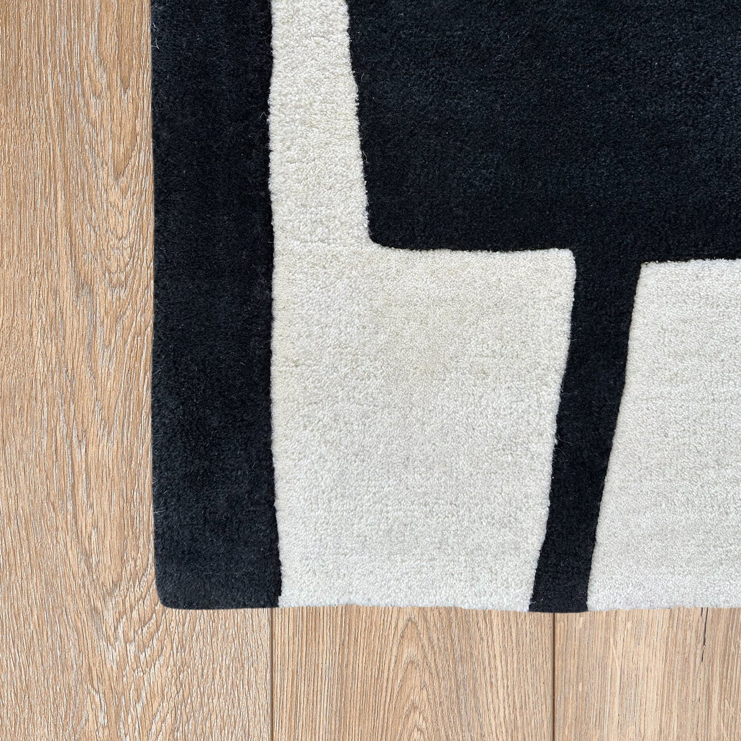 Close-up of a black, white, and gray geometric rug on a wooden floor.