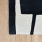 Close-up of a black, white, and gray geometric rug on a wooden floor.