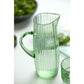 Green glass pitcher on a white surface with blurred greenery in the background