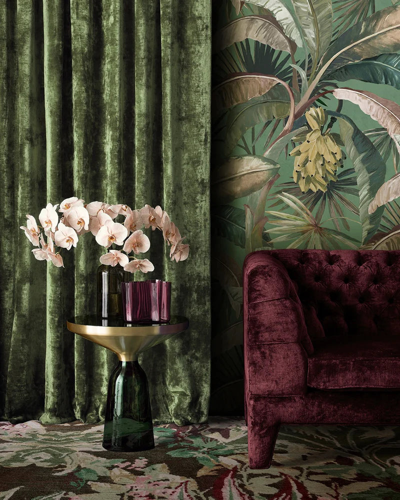 Decorative interior with green velvet curtains, floral arrangement, and burgundy sofa.