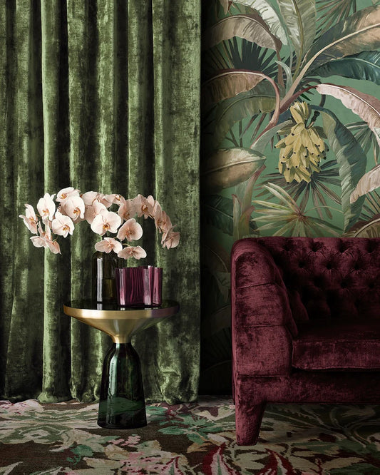 Decorative interior with green velvet curtains, floral arrangement, and burgundy sofa.