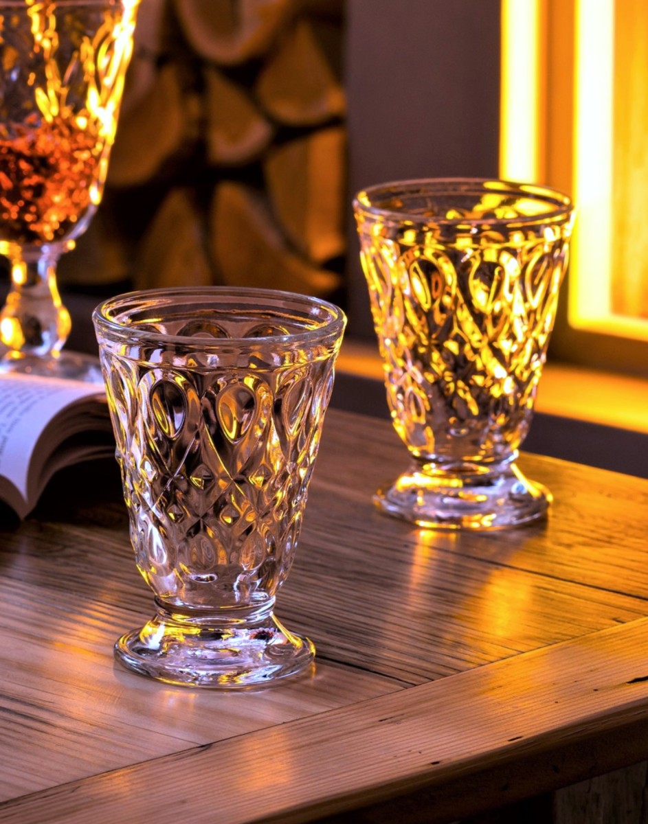 Two clear cut-crystal goblets with a diamond pattern, displayed on a rustic wooden table with warm ambient lighting.