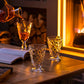 Person pouring a drink into a glass on a wooden table with a fireplace in the background