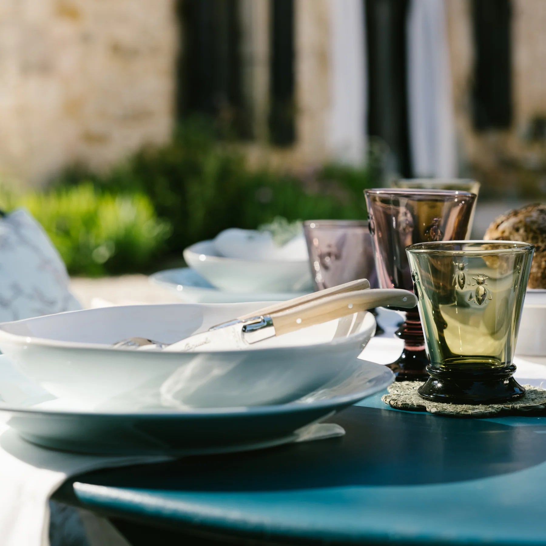 Dinnerware set on a table with glasses and cutlery outdoors