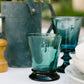 Teal glass with black base on a table with blurred background