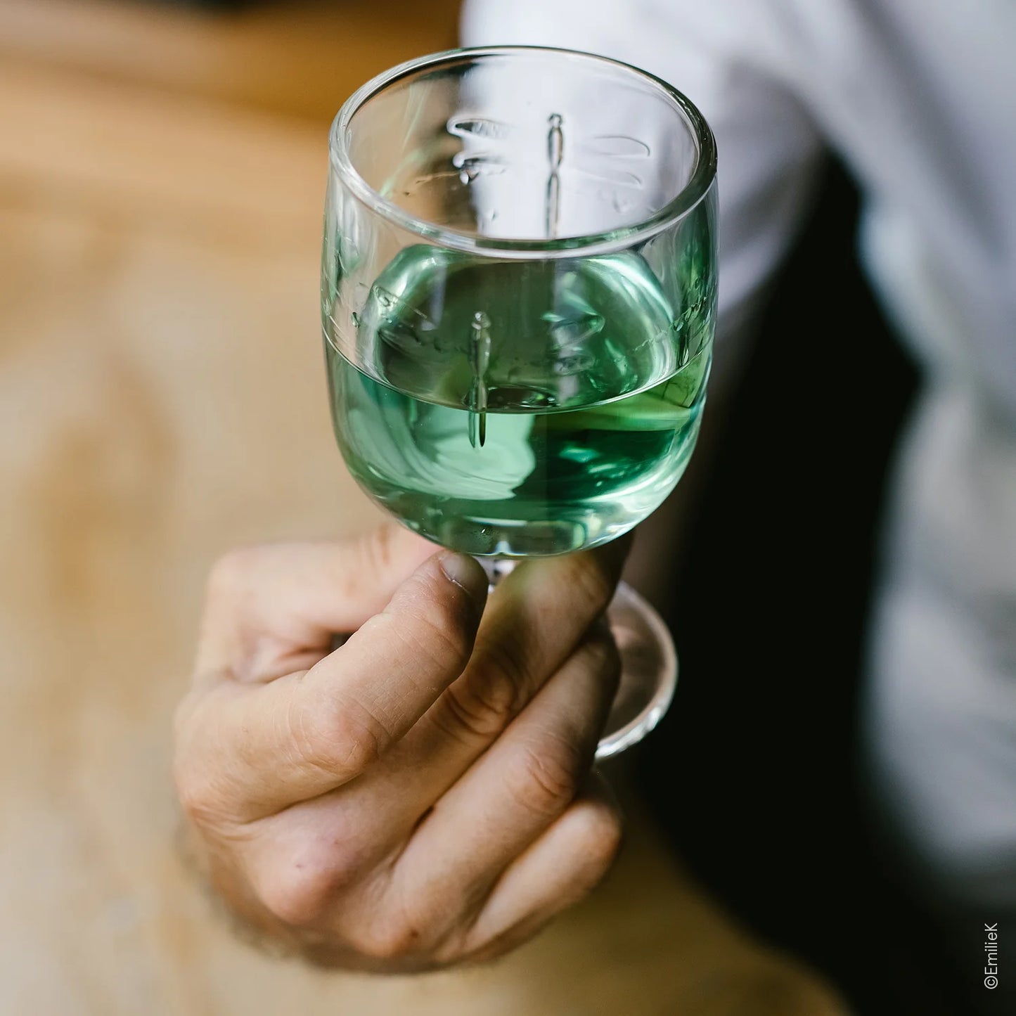 Hand holding a glass of green liquid with a blurred background