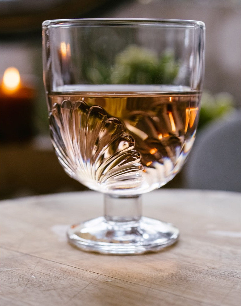 Glass of white wine on a wooden table with a blurred candle and plant in the background