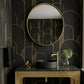 A luxury bathroom vanity setup featuring a gold-framed oval mirror, a black vessel sink, and a matching gold console table against a black wallpaper with gold geometric arch patterns.