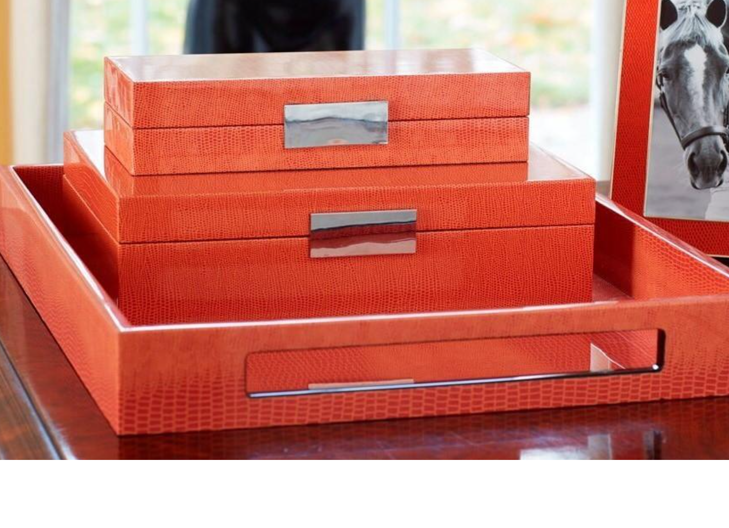 Set of orange decorative boxes with silver handles on a reflective surface.