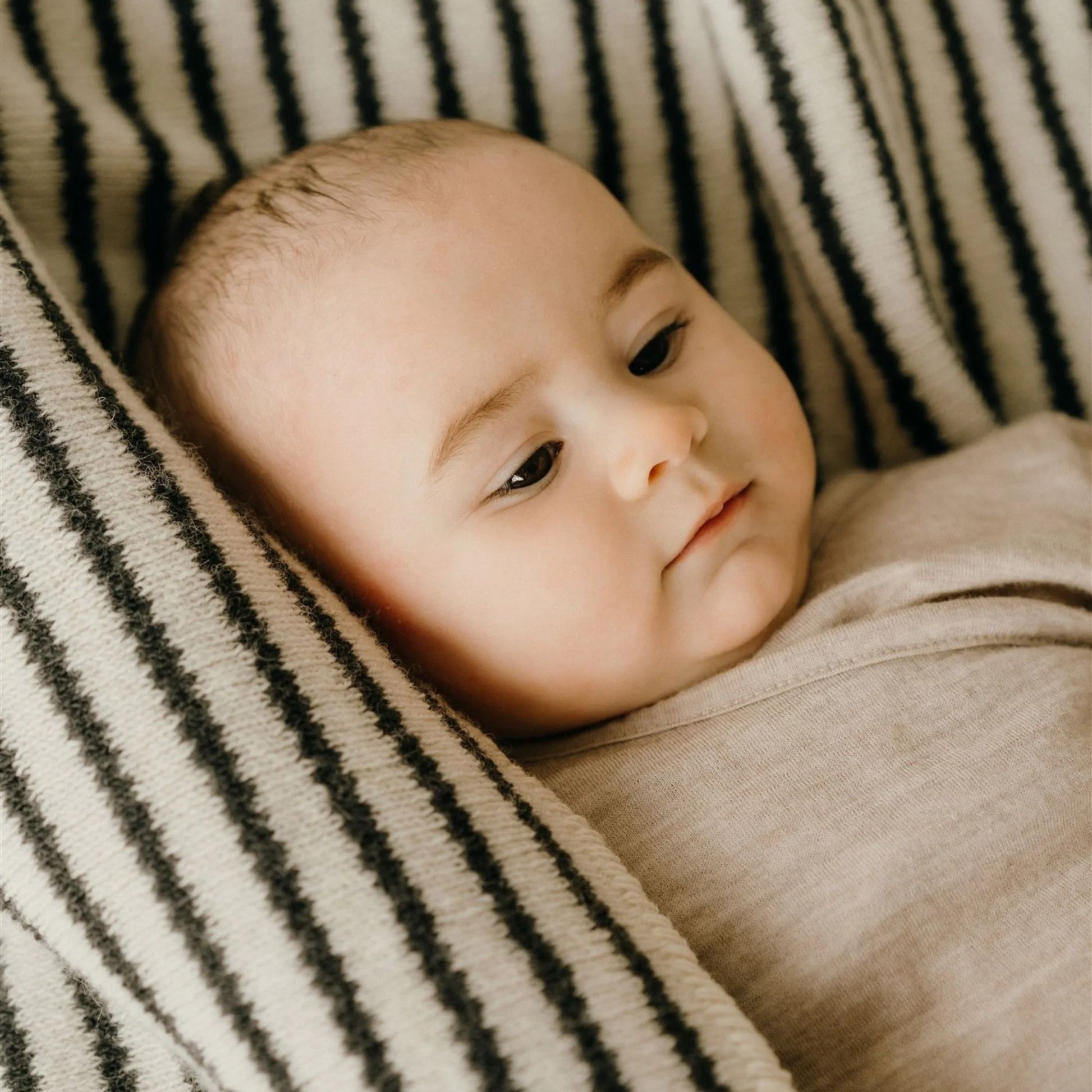 Baby wrapped in a beige blanket with a striped background