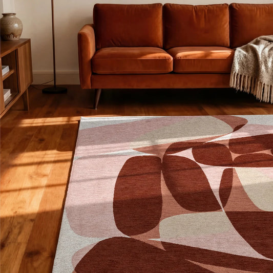 abstract rug with organic shapes in red, pink and clay on a wooden floor with a rust velvet sofa
