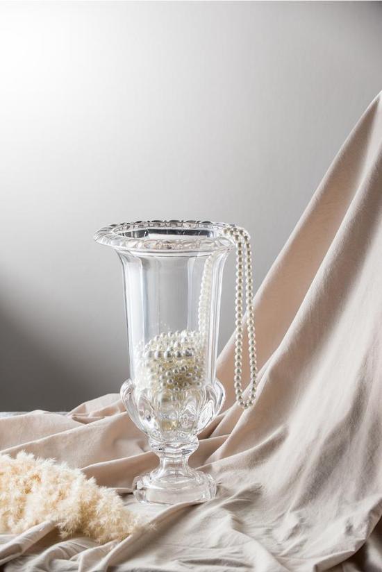 Clear glass vase with decorative elements on a draped fabric background