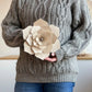 Person wearing a gray sweater holding a beige wooden flower.