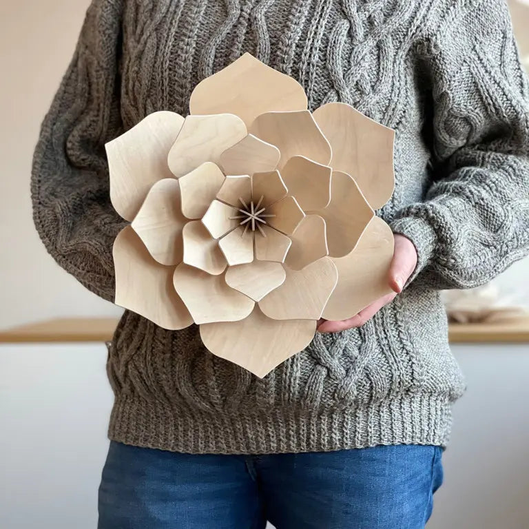 Person holding a large wooden paper flower against a neutral background