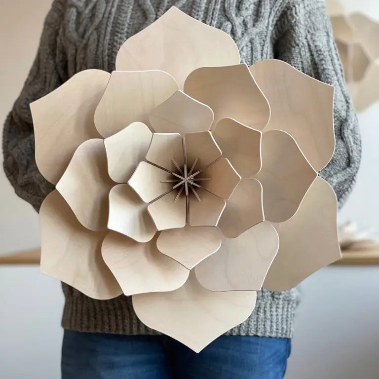 Large beige wooden flower held by a person wearing a gray sweater.